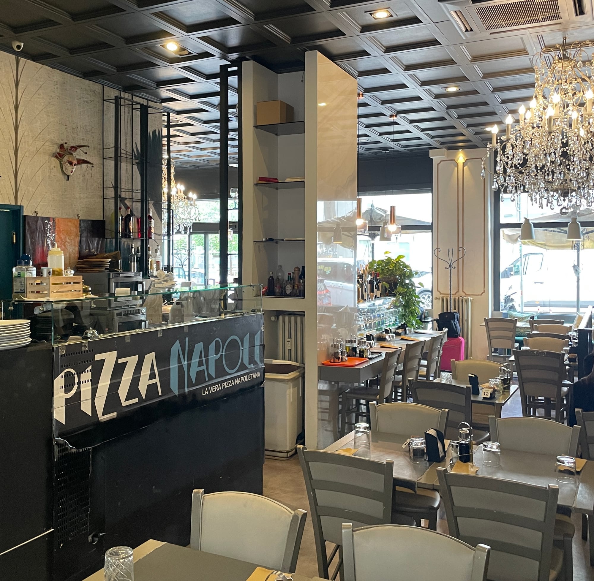 Interior of Pizzanapoli restaurant with tables, counter, and large windows looking onto the street