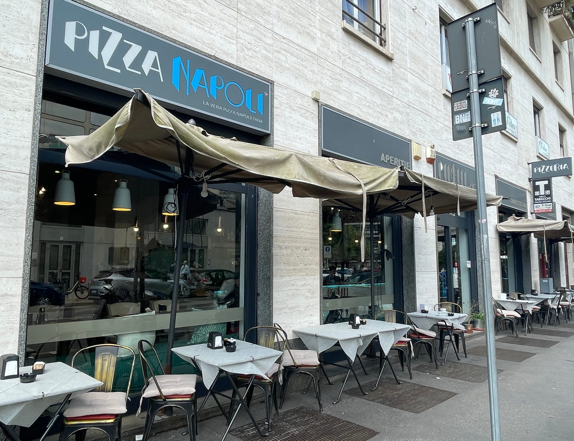 Pizzanapoli storefront with outdoor seating and cream awning on a European street