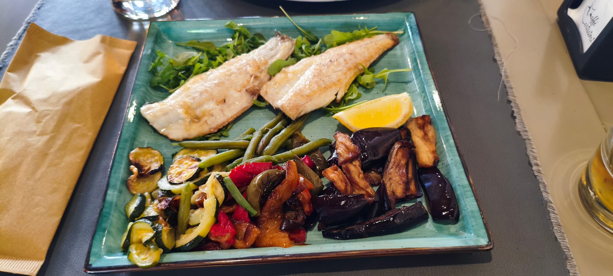 Pan-seared salmon with roasted vegetables and a lemon wedge on a teal ceramic plate